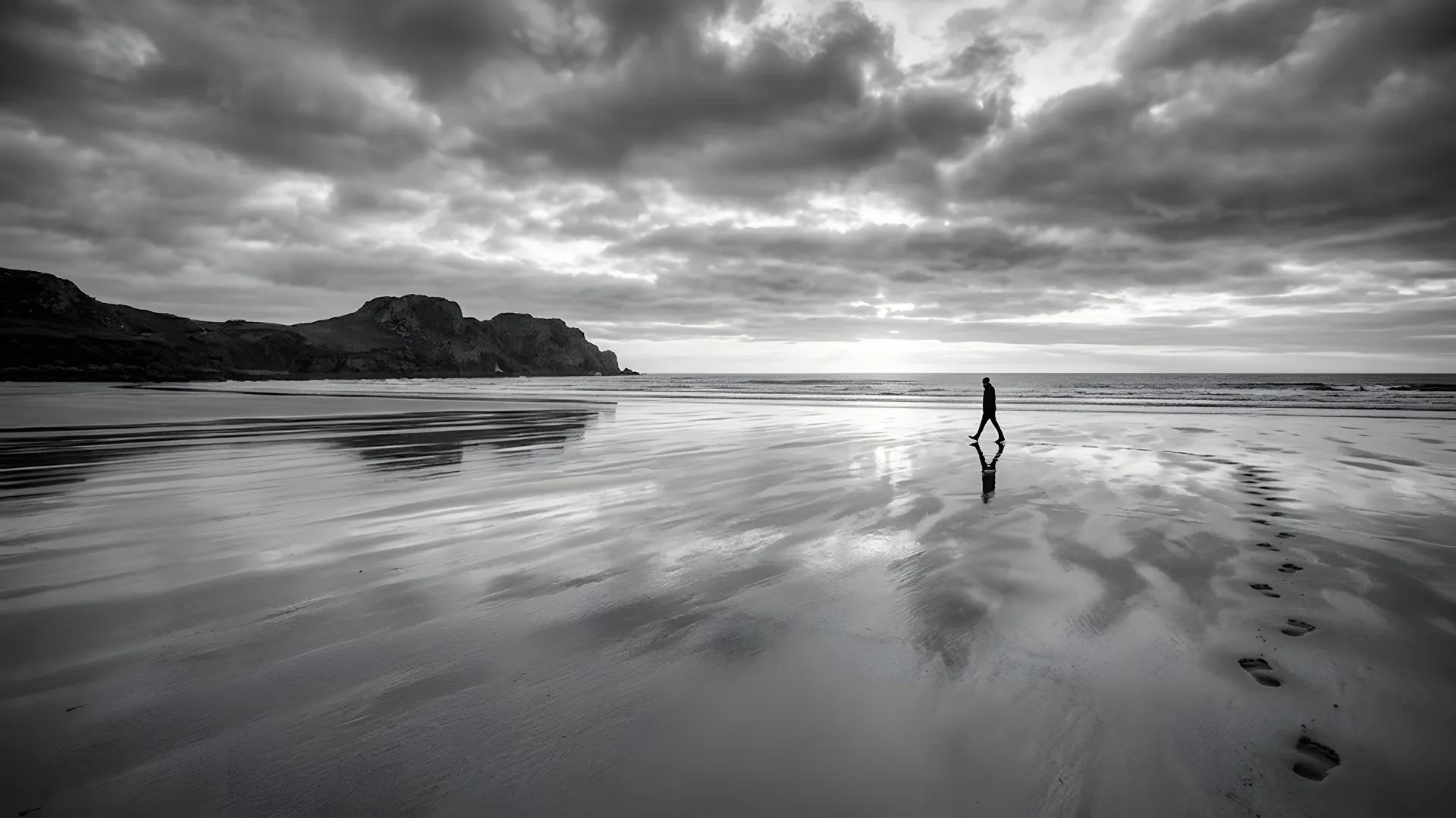 A lone figure walking along a wet beach, leaving footprints